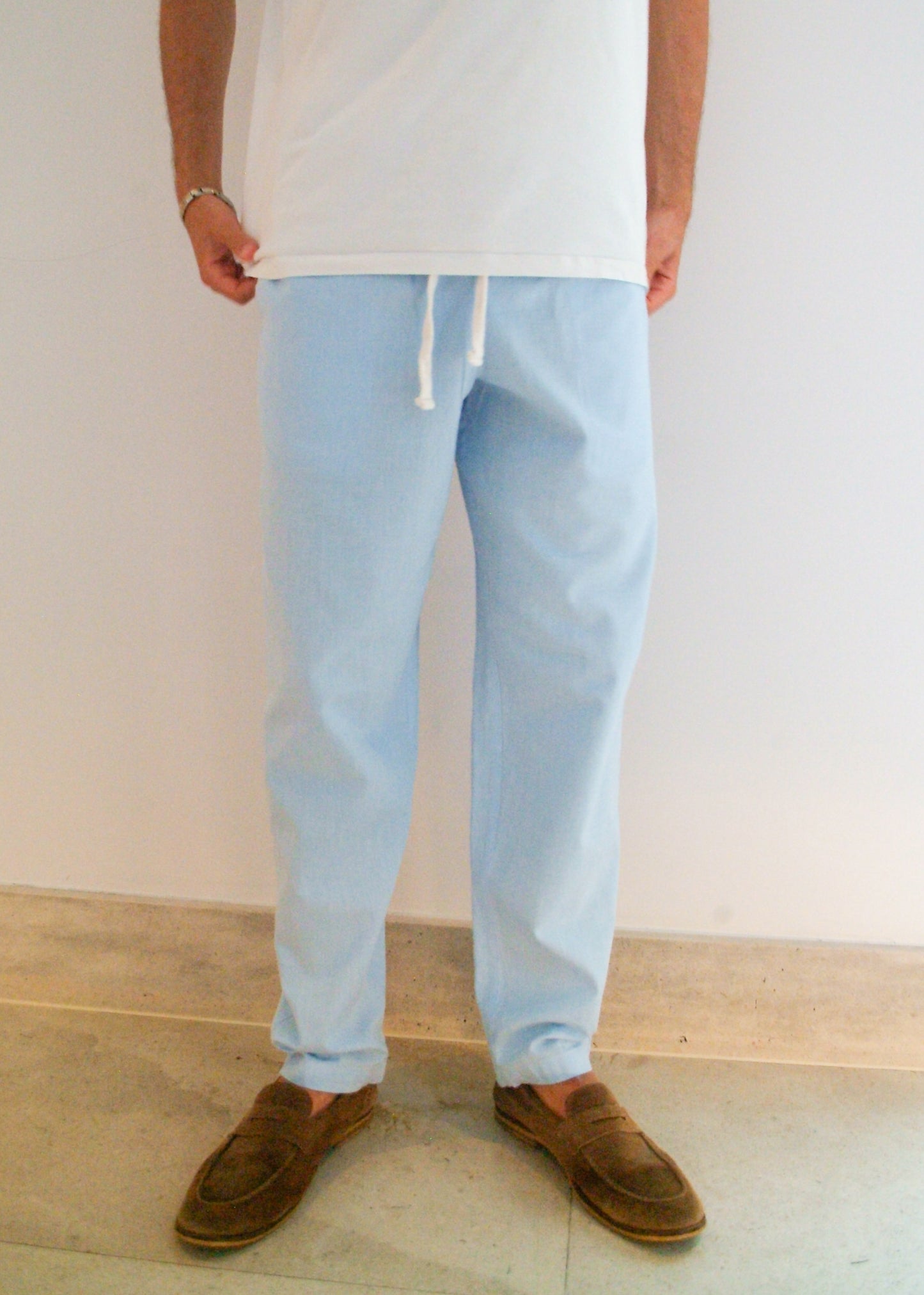 Person wearing light blue pants and brown shoes against a plain background