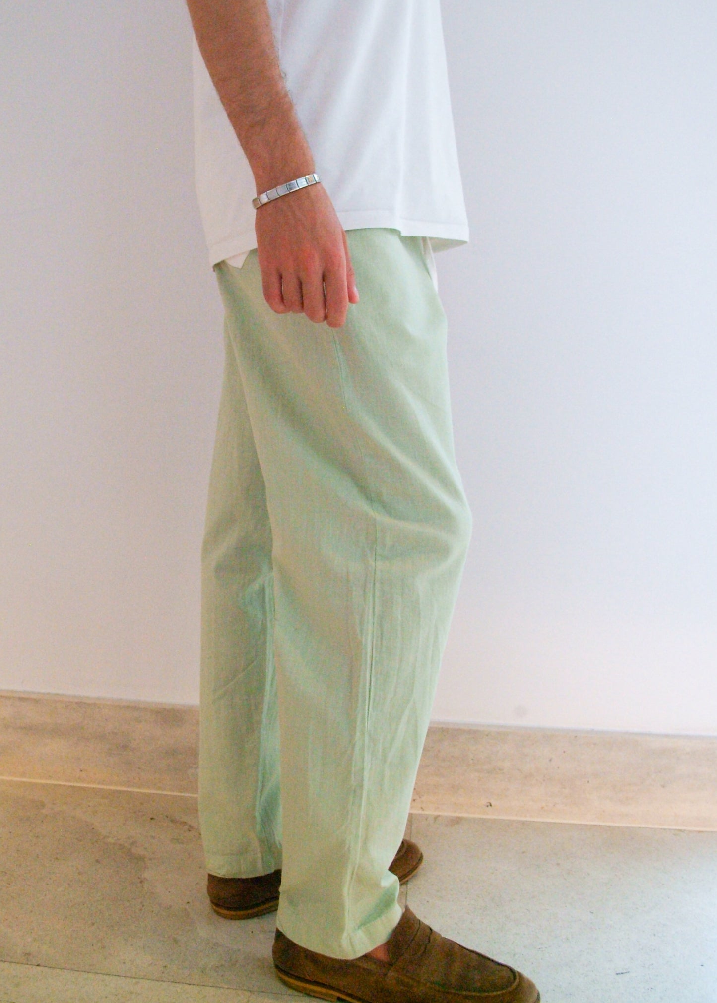 Person wearing light green pants and a white shirt against a plain background