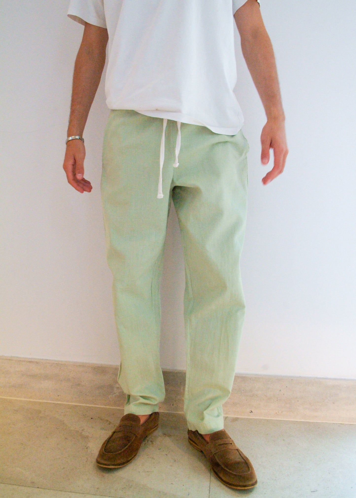 Person wearing light green pants and brown shoes against a white wall.