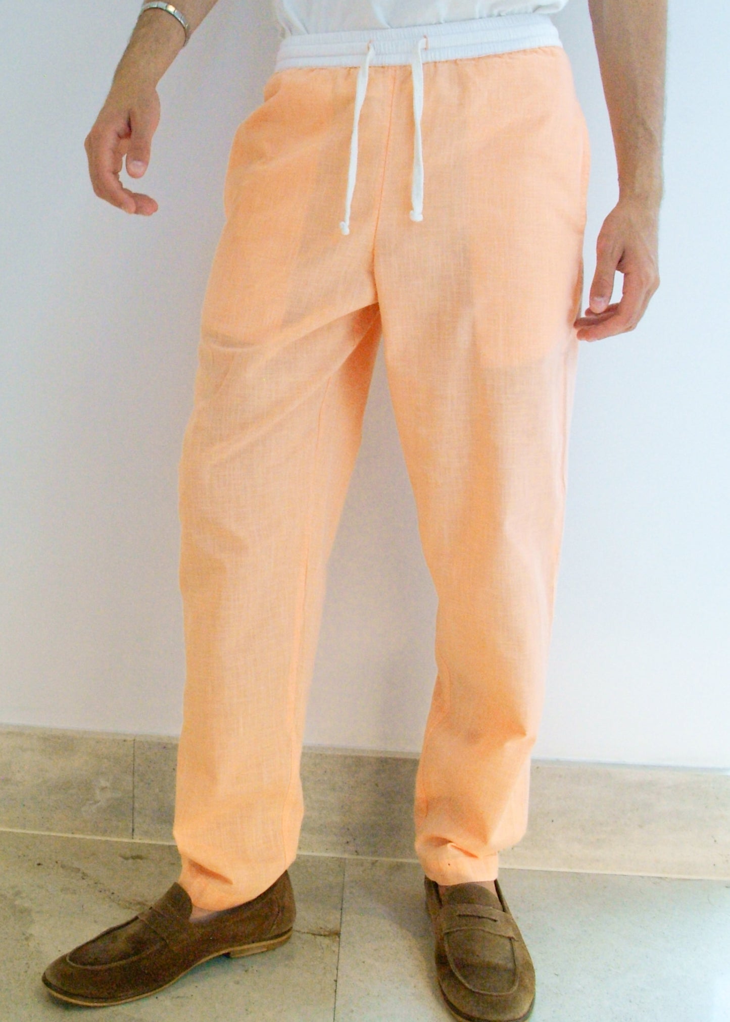 Person wearing peach-colored pants with a white top against a plain background