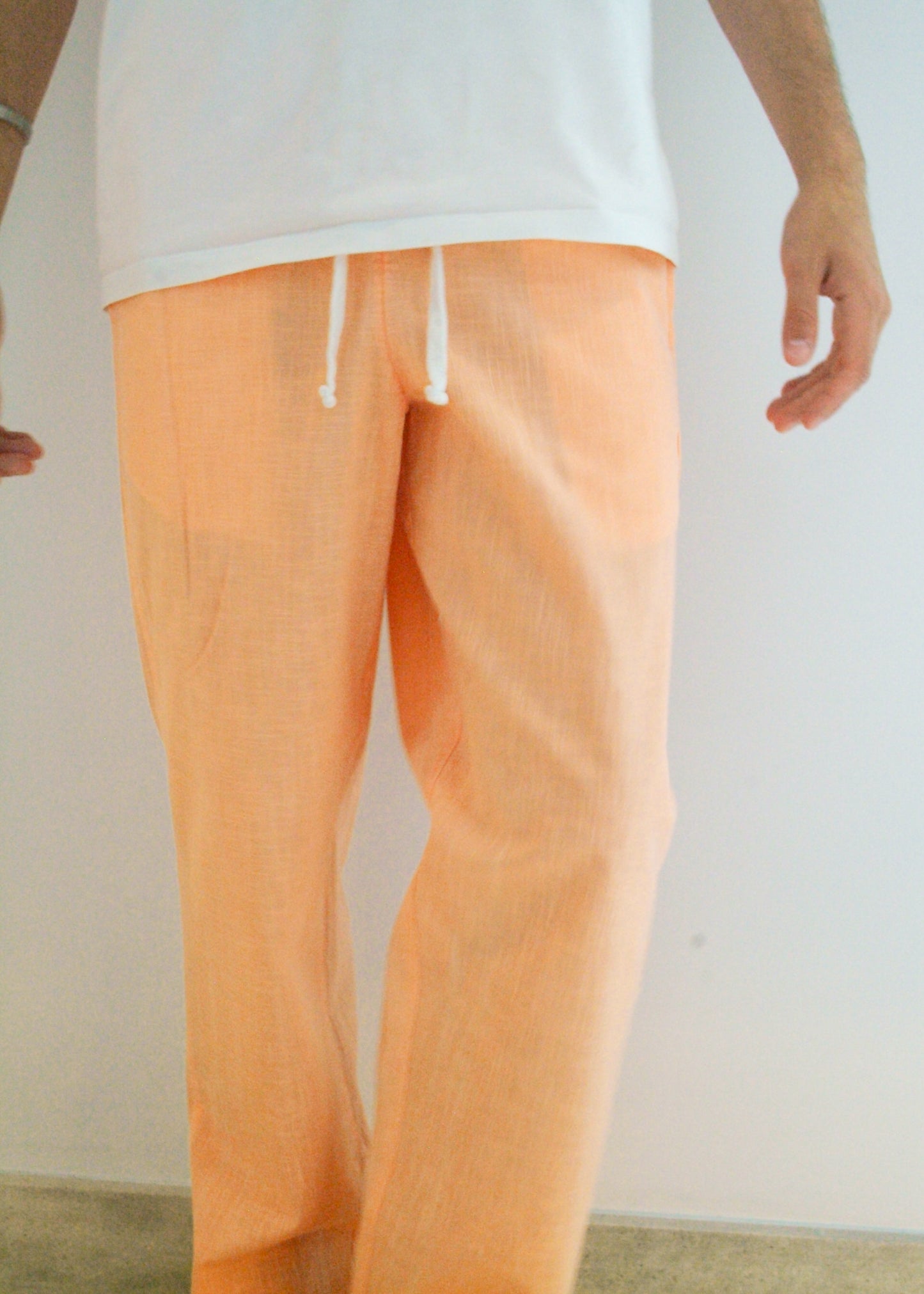 Person wearing peach-colored pants and a white top against a plain background