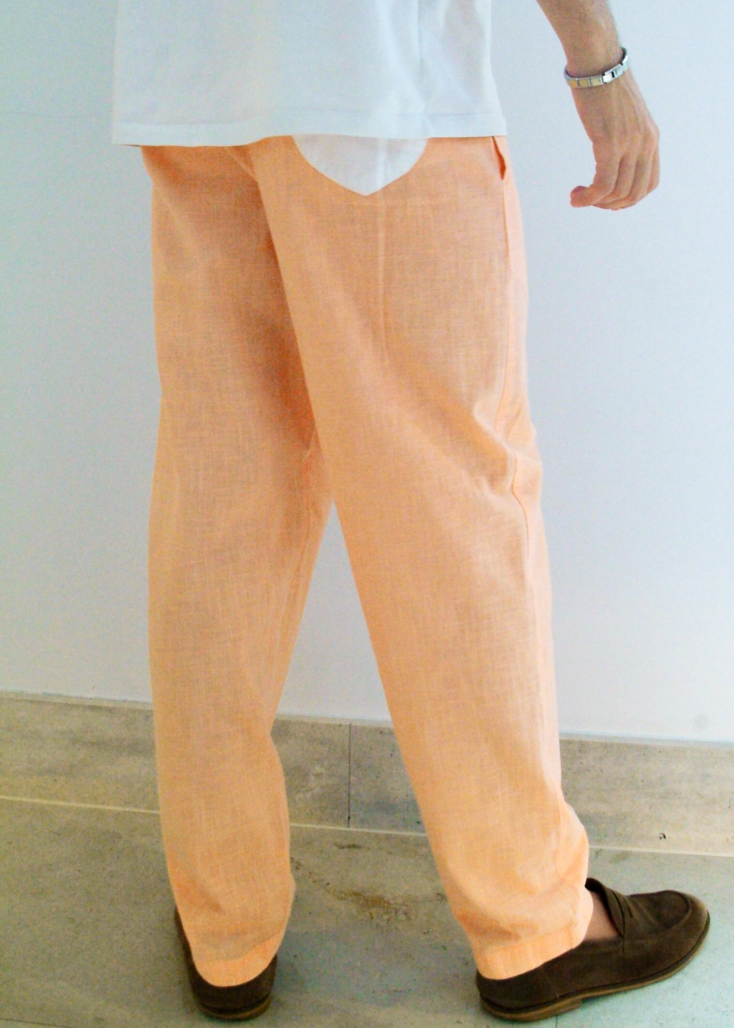 Person wearing peach pants and a white shirt against a plain background