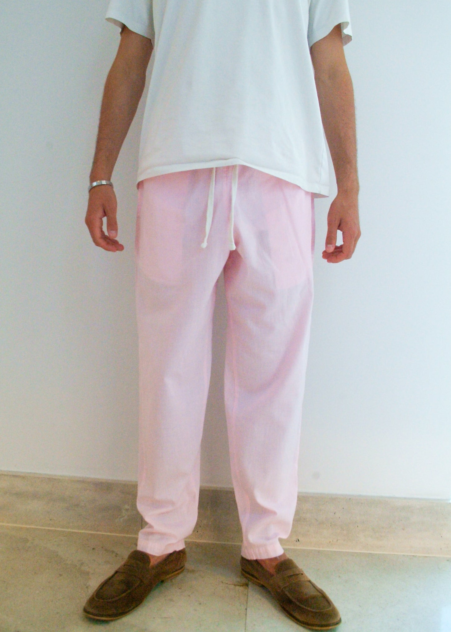 Person wearing light pink pants and a white shirt against a plain background