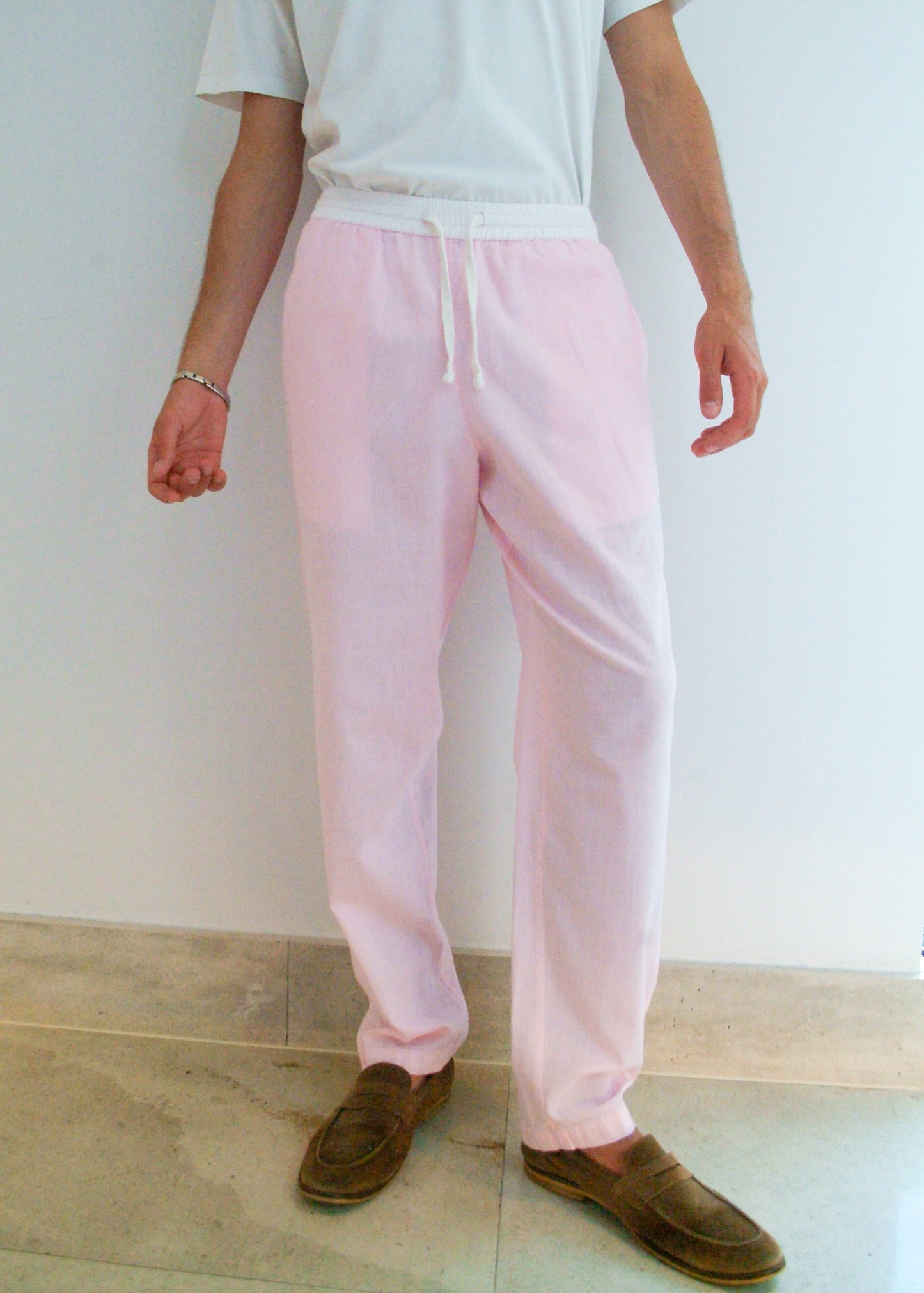 Person wearing light pink pants and brown shoes against a white wall.