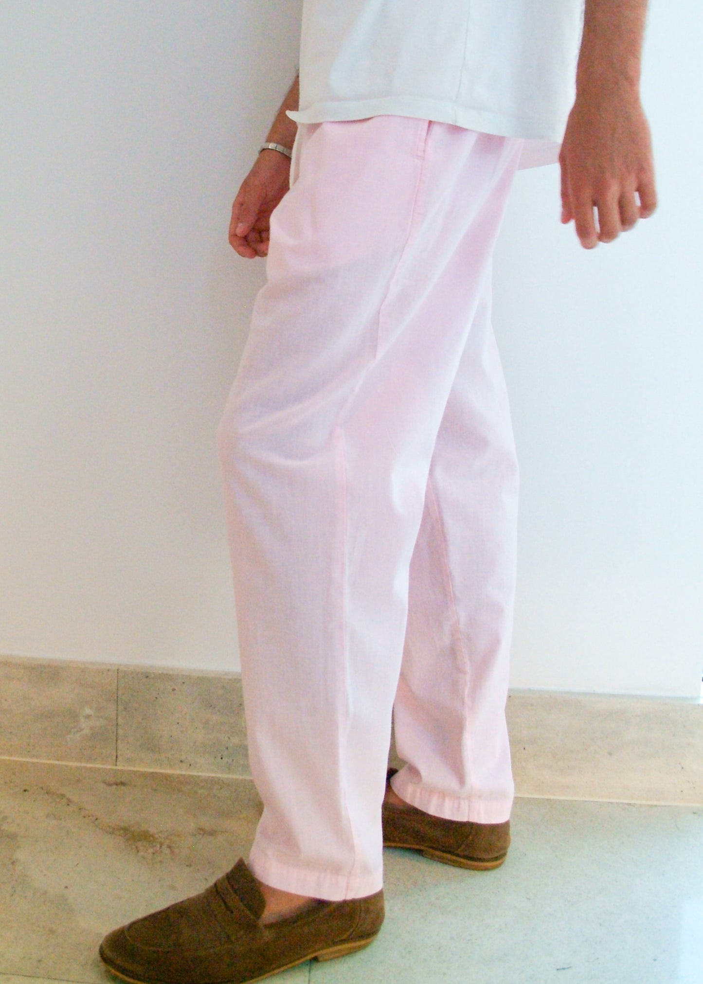Person wearing light pink pants and brown shoes against a white wall.