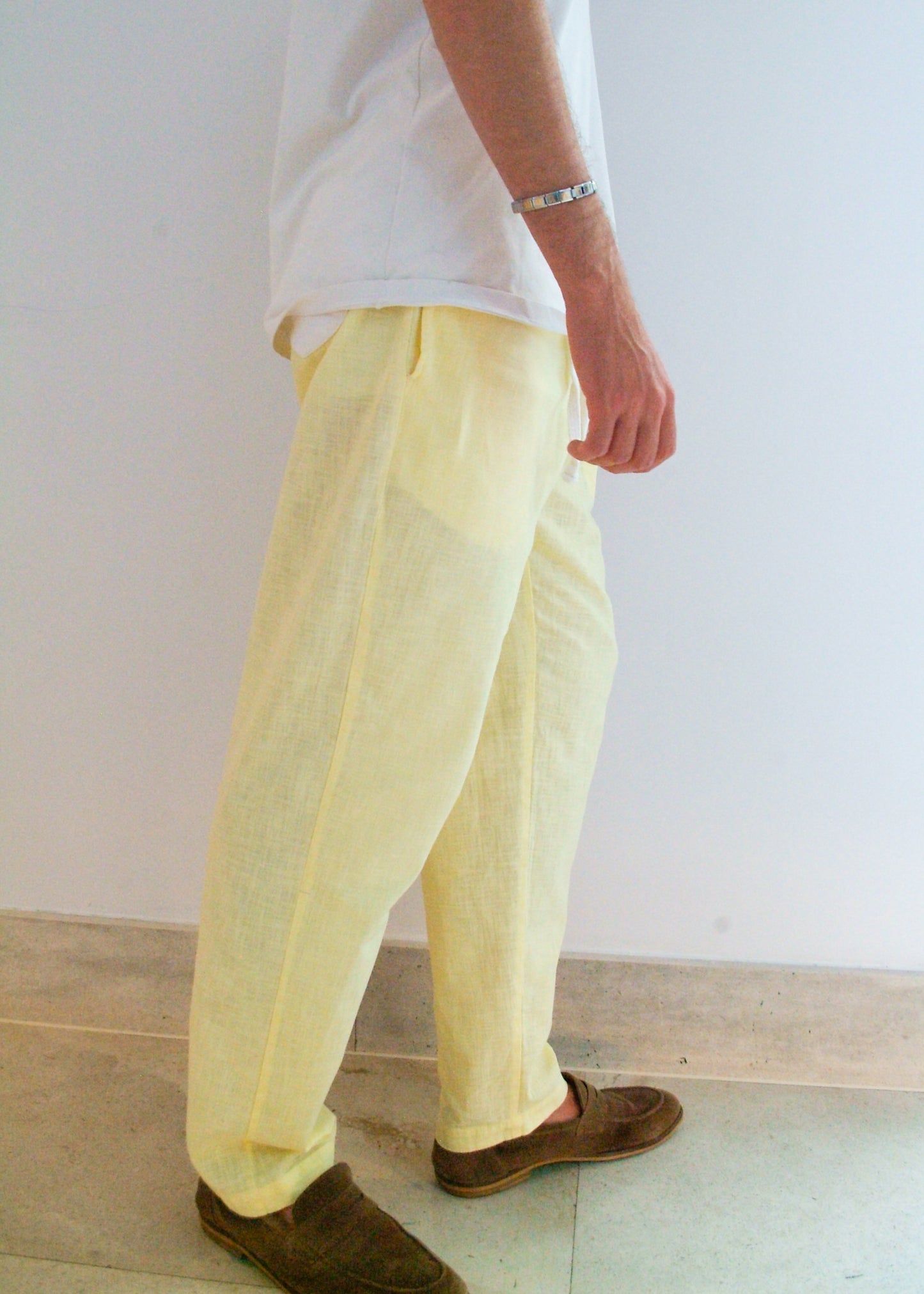 Person wearing light yellow pants and brown shoes against a white wall.
