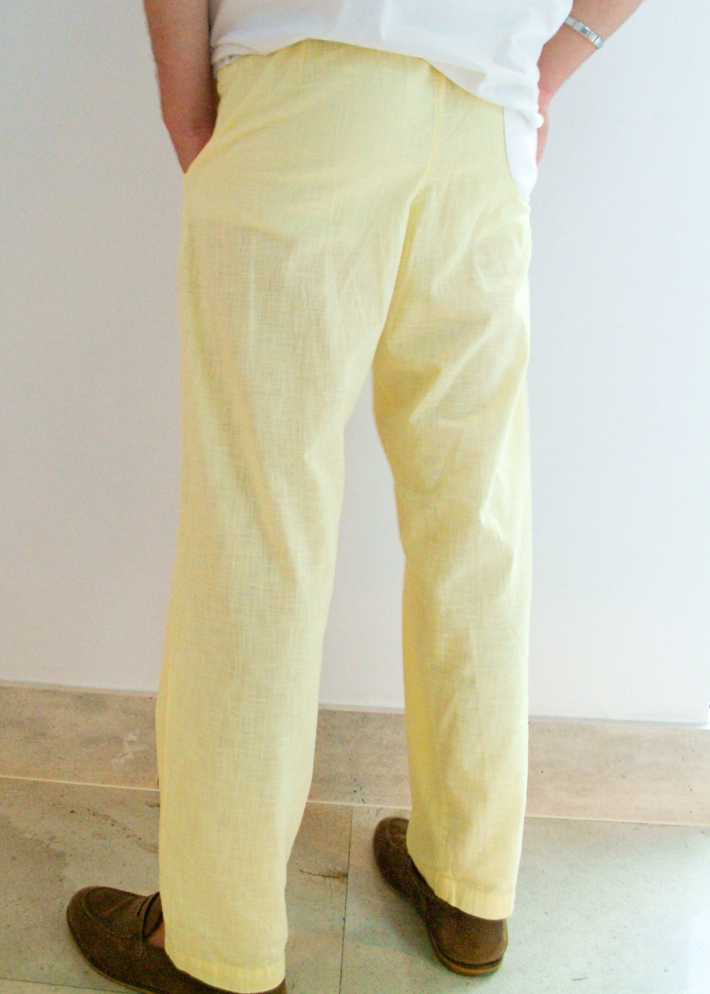 Person wearing light yellow pants and brown shoes on a plain background