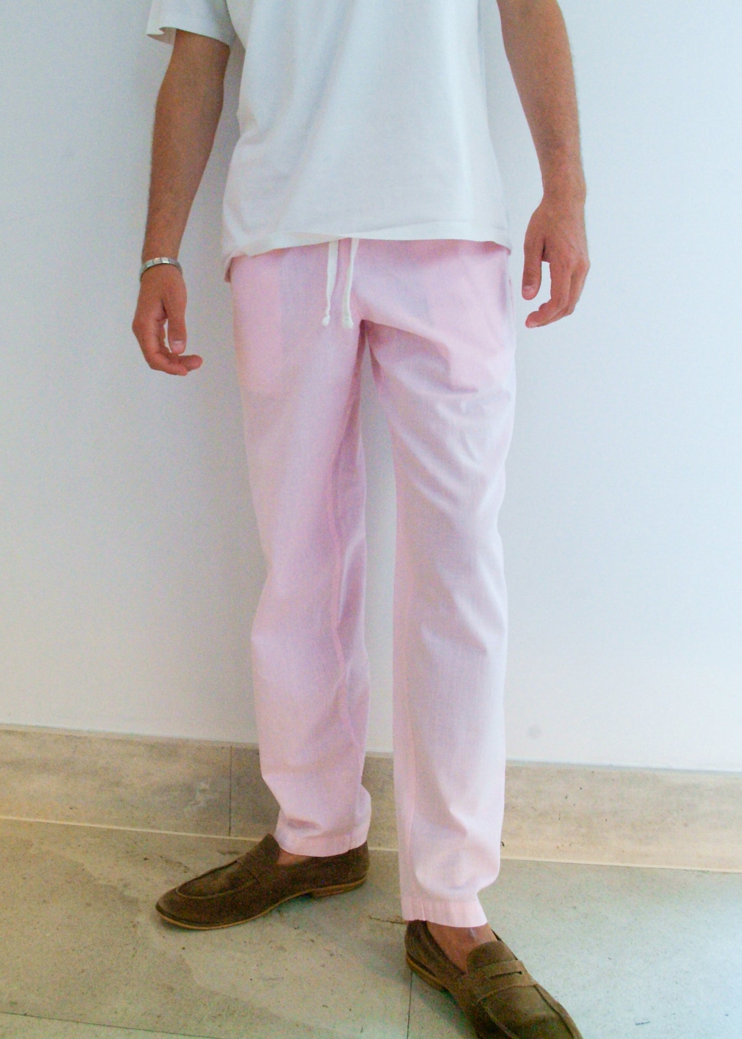 Person wearing capts daughter light pink pants and brown shoes against a white wall.