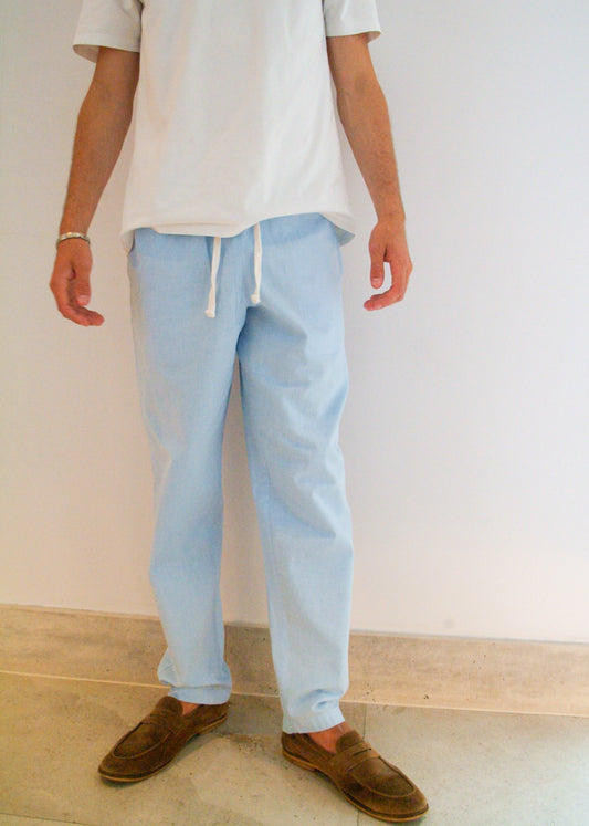 Person wearing a white shirt and light blue pants against a plain wall.