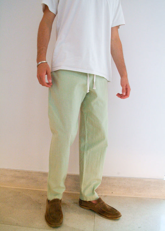 Person wearing light green pants and a white shirt against a plain background