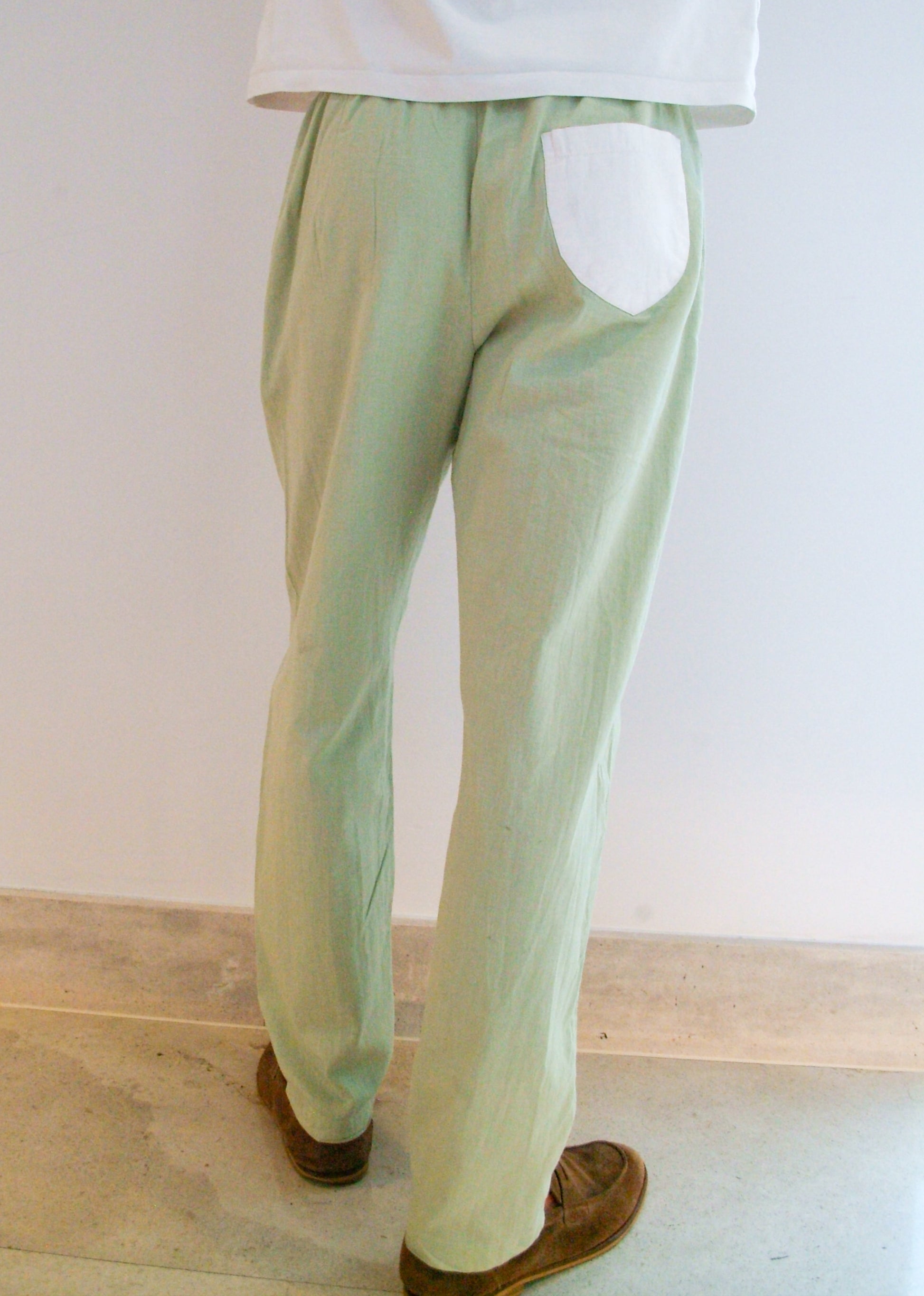Person wearing light green pants and a white shirt on a plain background