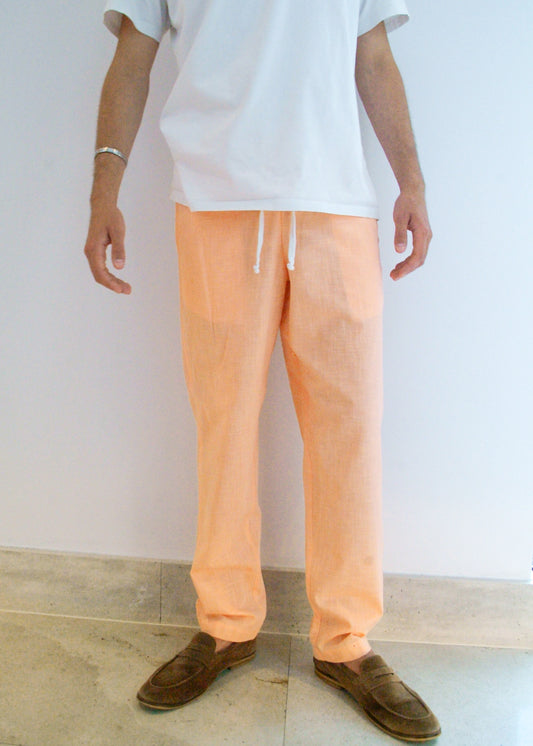 Person wearing peach pants and brown shoes against a white wall.