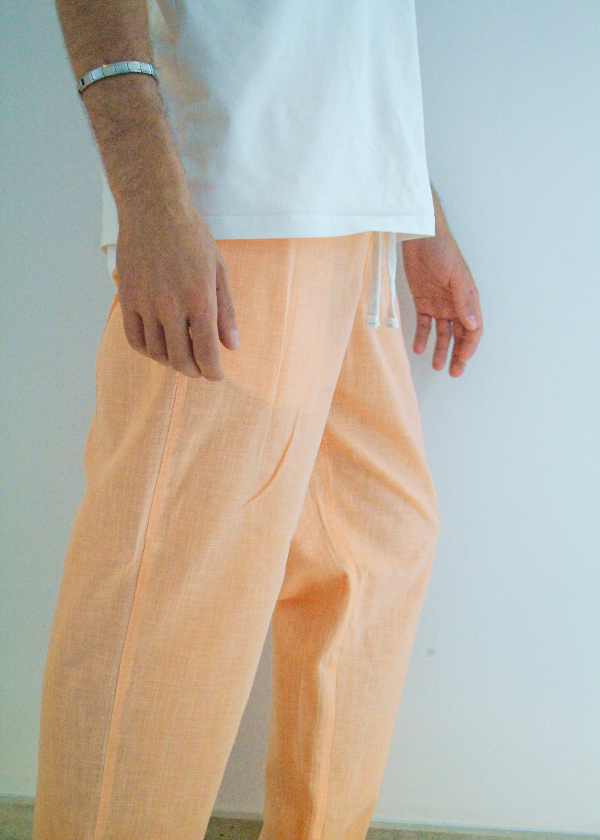 Person wearing peach pants and a white shirt against a plain background