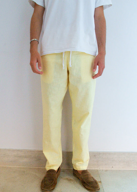 Person wearing light yellow pants and a white shirt against a plain background